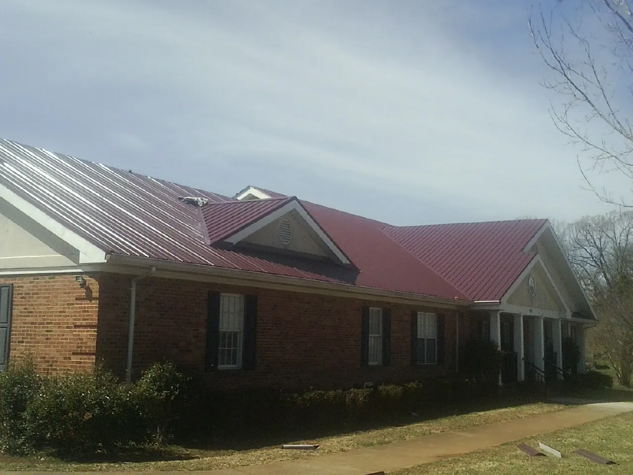 Red metal roof with gabled entries on a long brick building, from a Hail Damage Roof Repair job in Tyler