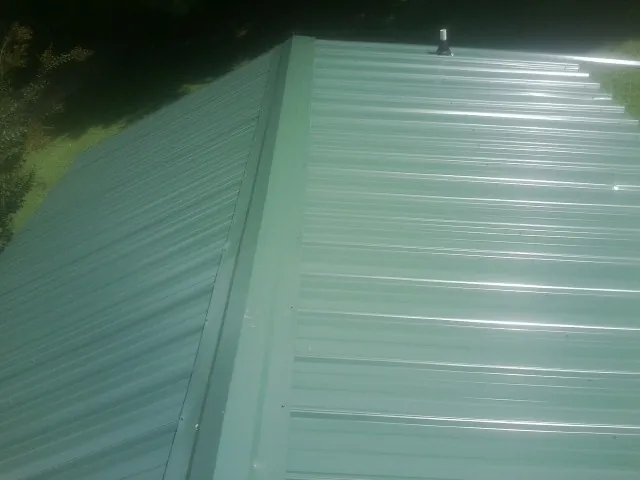 New green metal panels meeting at the ridge of a roof — Flat Roof Repair work by our crew in Tyler