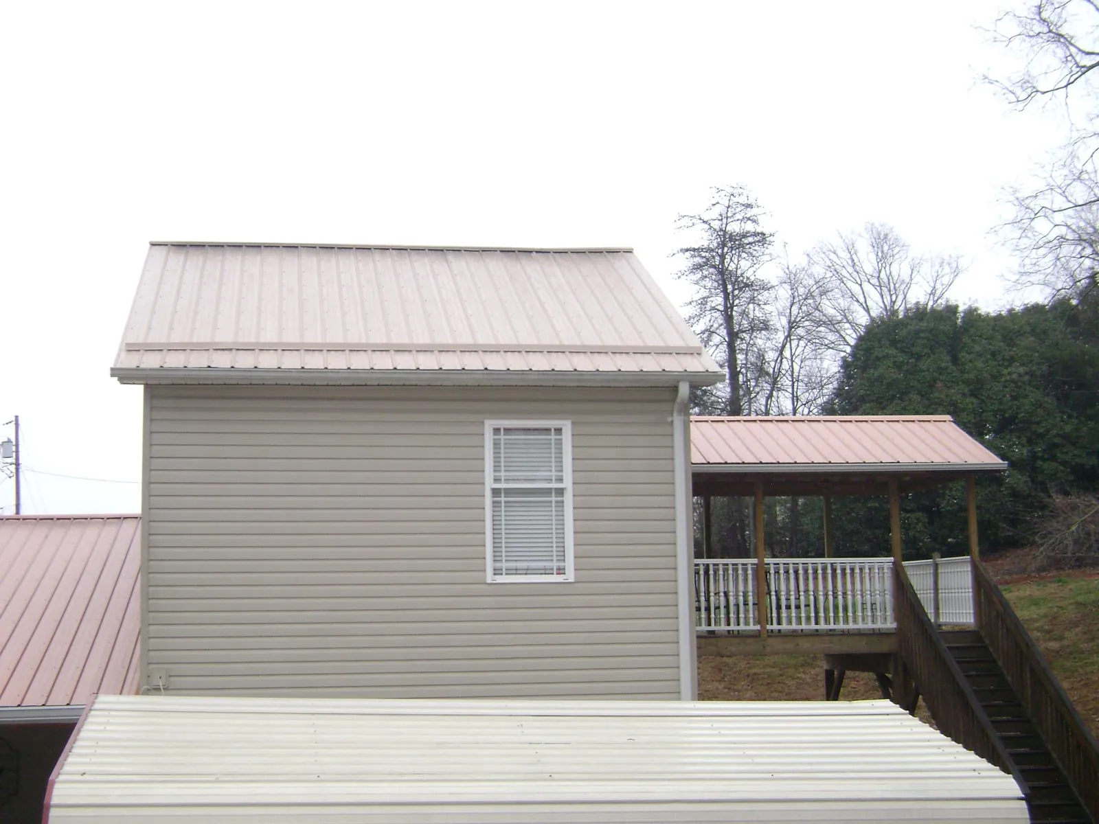 Tan metal roofs on a two story addition and attached porch, from a Roof Replacement job in Tyler
