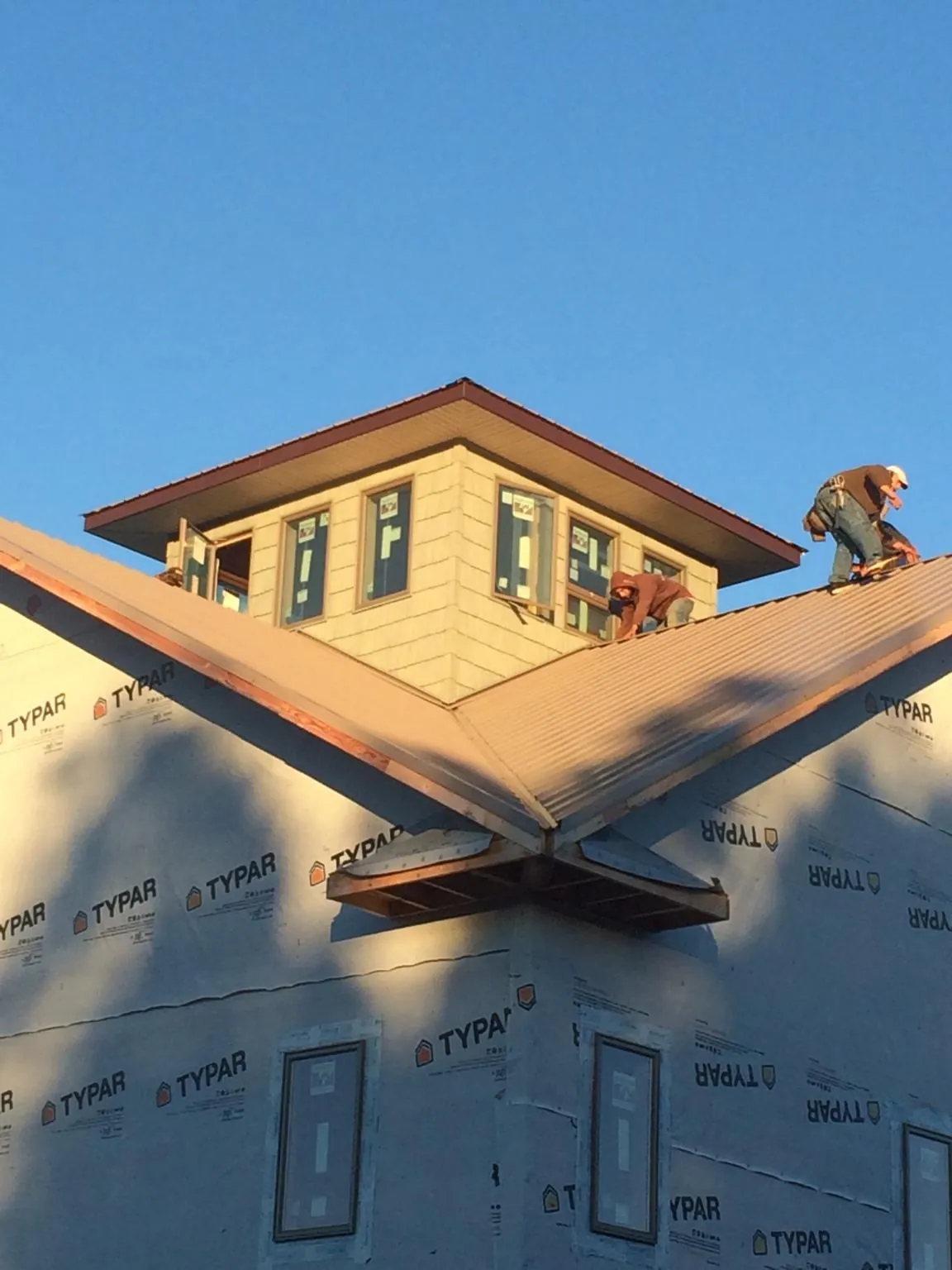 Roofers working around a rooftop cupola on a new metal roof at sunset — Roof Waterproofing in Tyler by Roofing Brothers